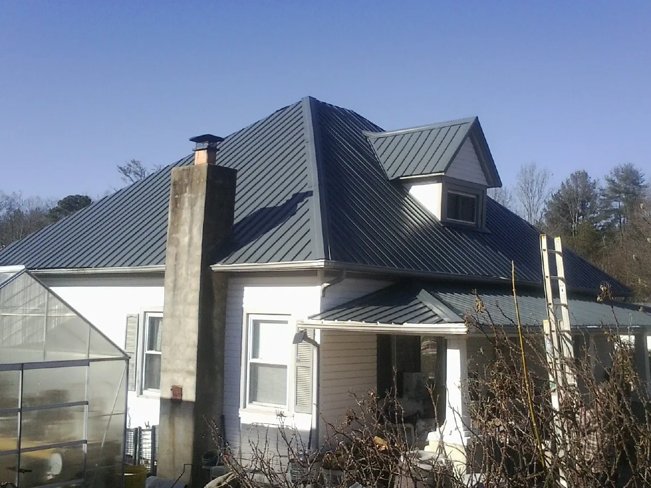 Dark blue standing seam metal roof on a white farmhouse with dormer — Slate & Tile Roof Repair by Roofing Brothers in Bovey