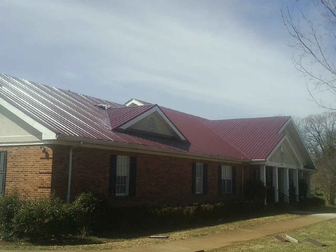 Red metal roof with gabled entries on a long brick building, from a Hail Damage Roof Repair job in Bovey