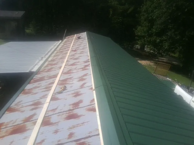 Old rusted panels beside newly installed green metal roofing — Wind Damage Roof Repair by Roofing Brothers in Bovey