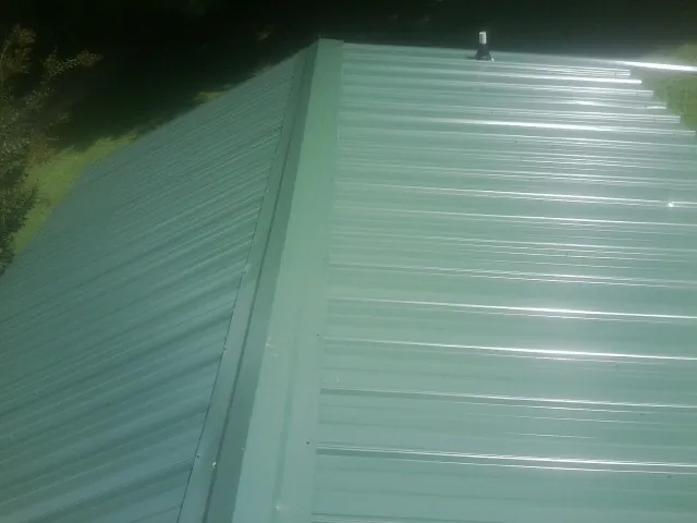 New green metal panels meeting at the ridge of a roof — Flat Roof Repair work by our crew in Bovey
