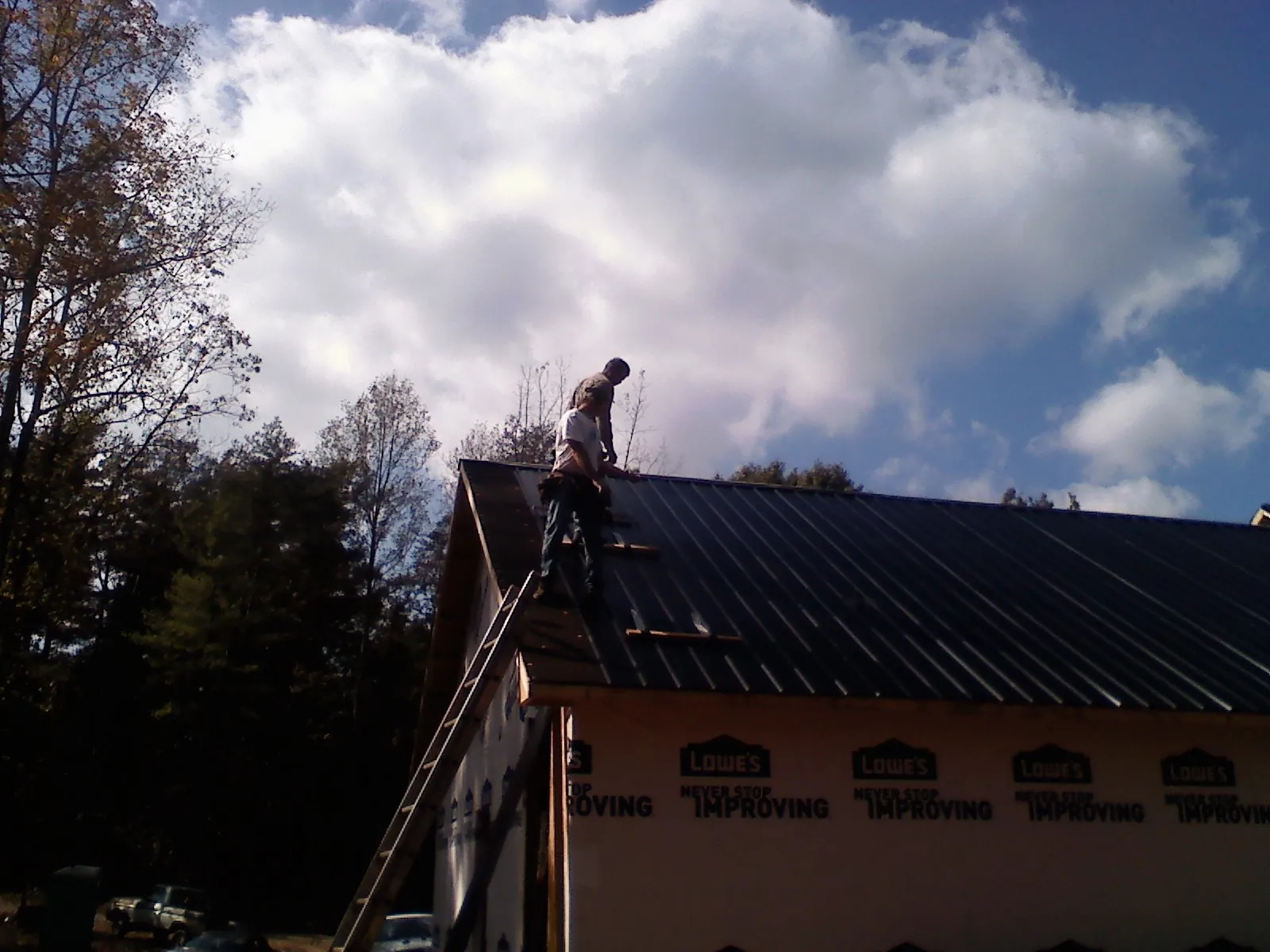 Roofer fastening dark metal panels high against a cloudy sky, from a Roof Inspection job in Bovey