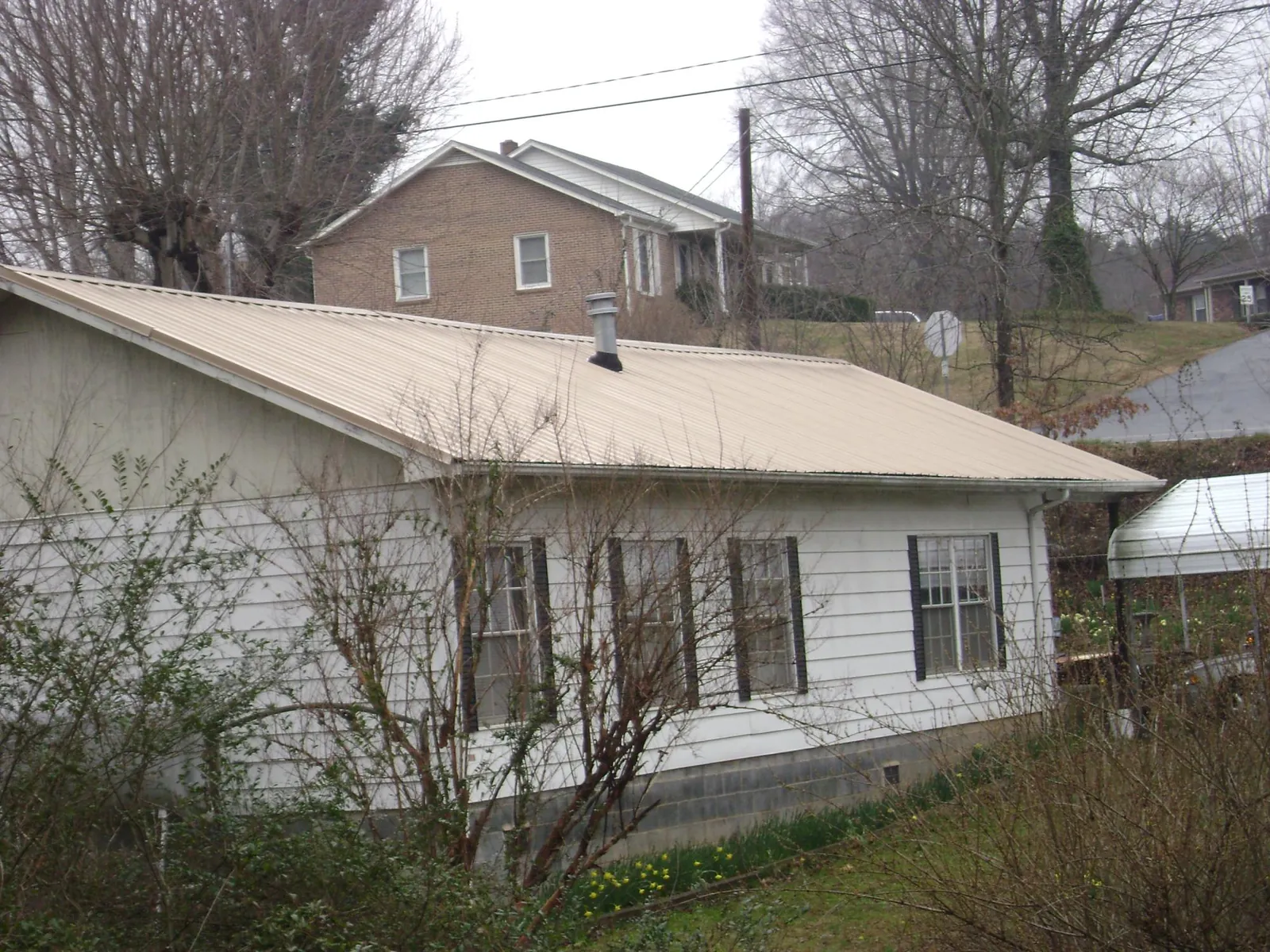 Tan metal roof on a white sided house set into a hillside — Commercial Roofing by Roofing Brothers in Bovey