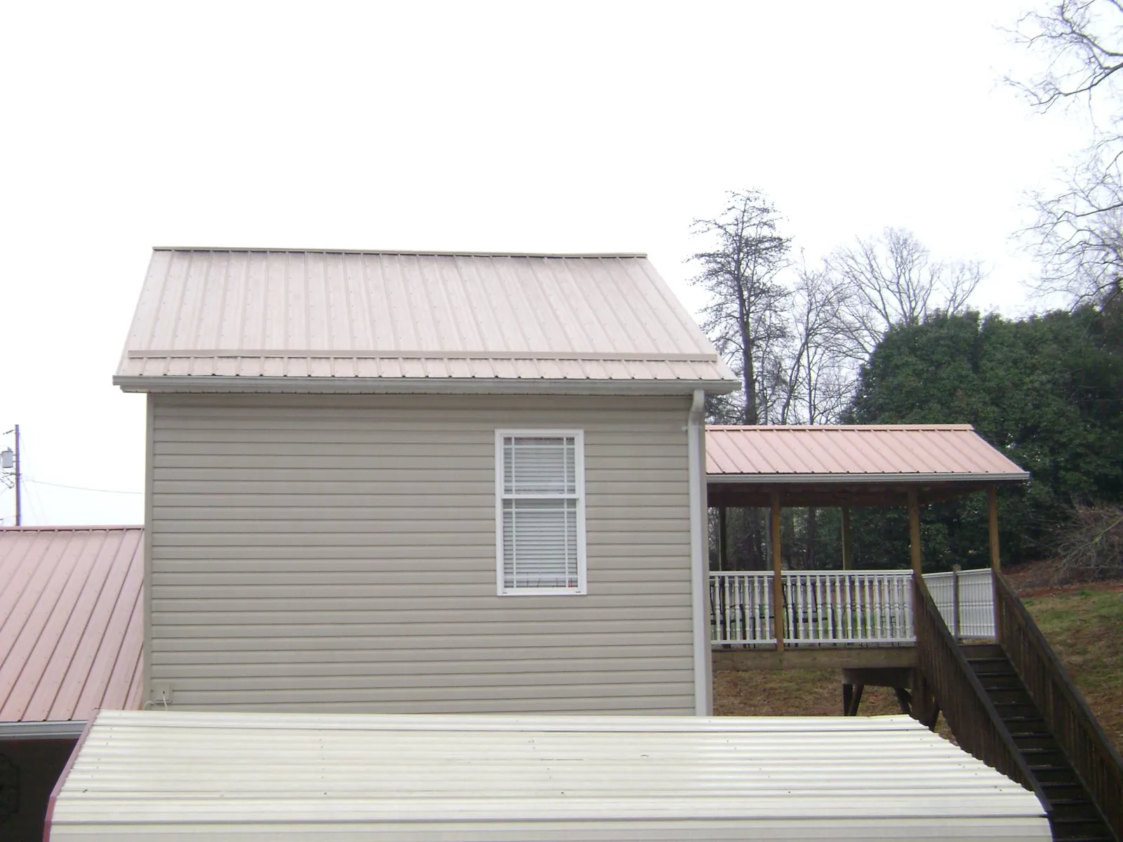 Tan metal roofs on a two story addition and attached porch, from a Roof Replacement job in Bovey